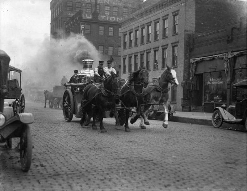 A historic horse-drawn steam fire engine moving along a Baltimore street